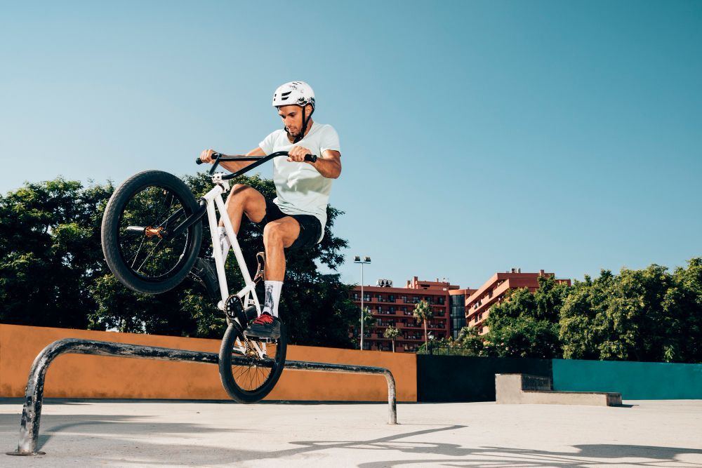 BMX rider popping a wheelie over a rail at an outdoor skatepark