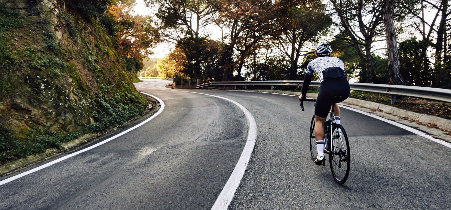 Road cyclist riding around a bend on a tree-lined country road