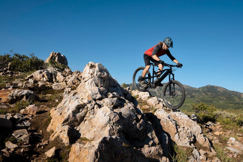 Mountain biker riding over a rocky outcrop on a sunny hillside trail