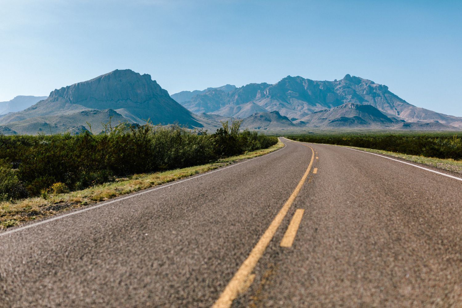 Empty two-lane road with a yellow center line leading toward rocky mountains